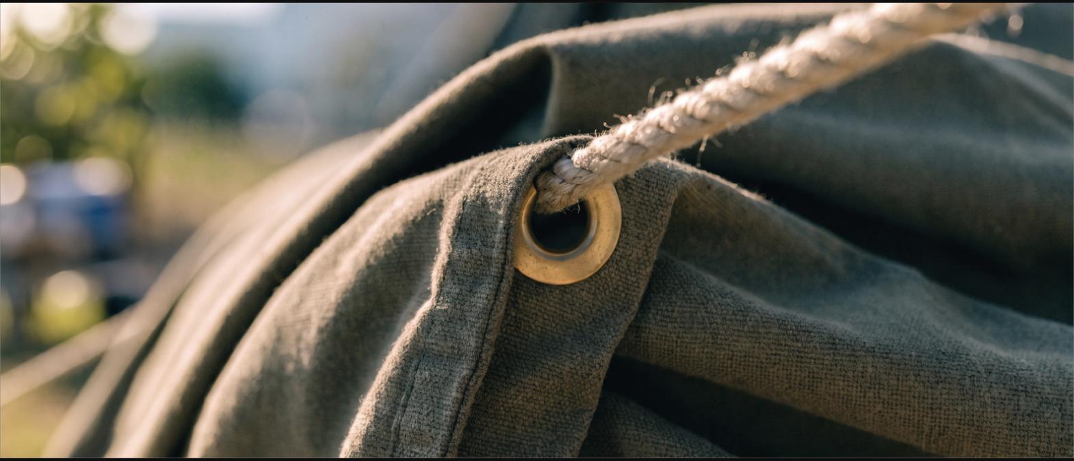 Close-up of heavy canvas with a reinforced seam, brass grommet and taut guy line